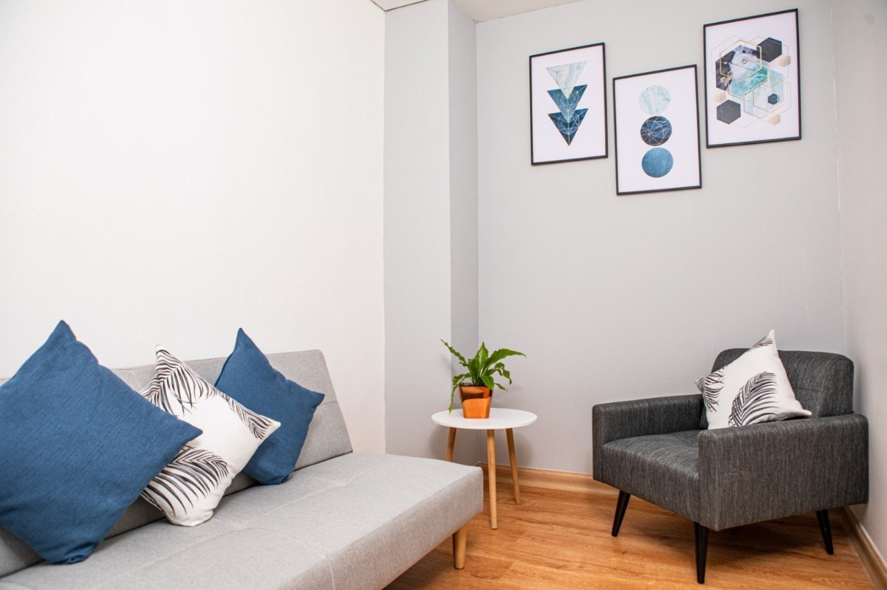 Sala terapéutica con sofá claro, sillón gris y cojines azules