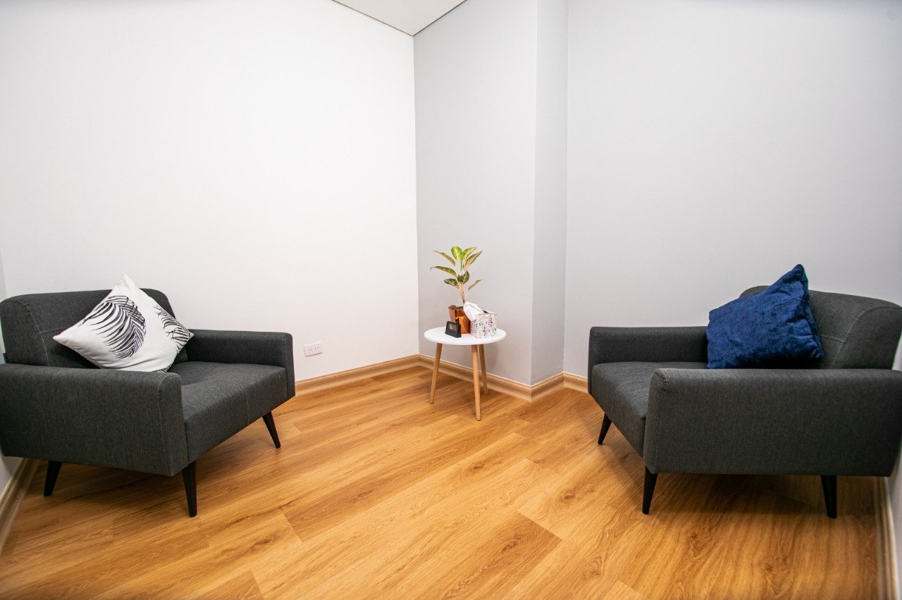 Consultorio con dos sillones grises enfrentados y mesa auxiliar