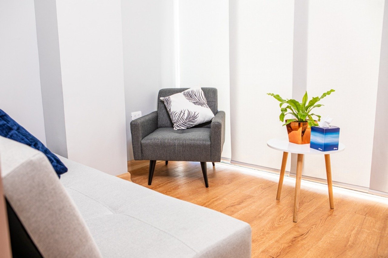 Detalle de consultorio con sillón, sofá, planta y mesa auxiliar